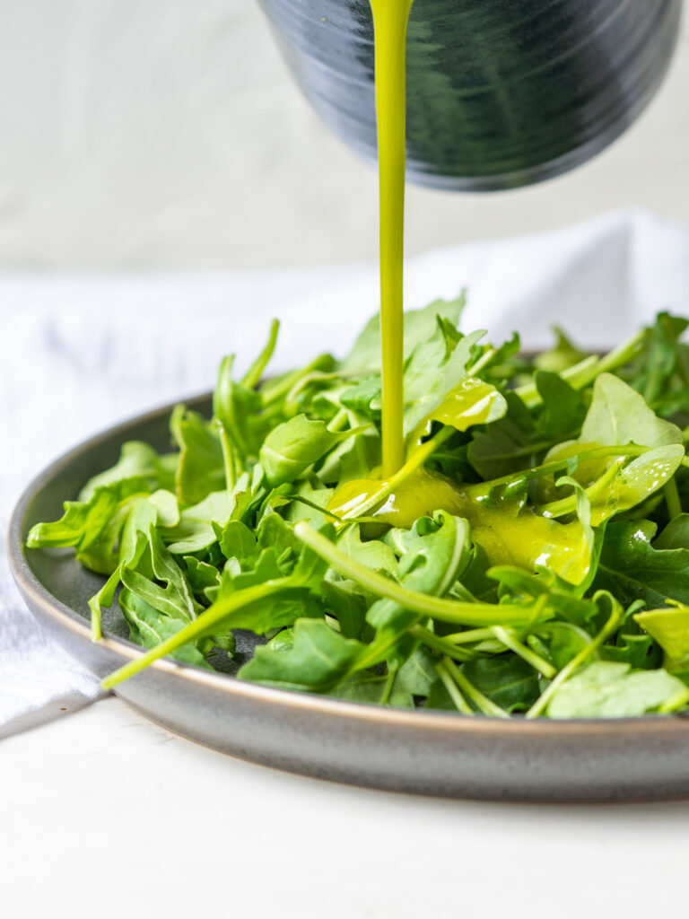 Healthy lemon herb salad dressing pouring onto a bed of greens