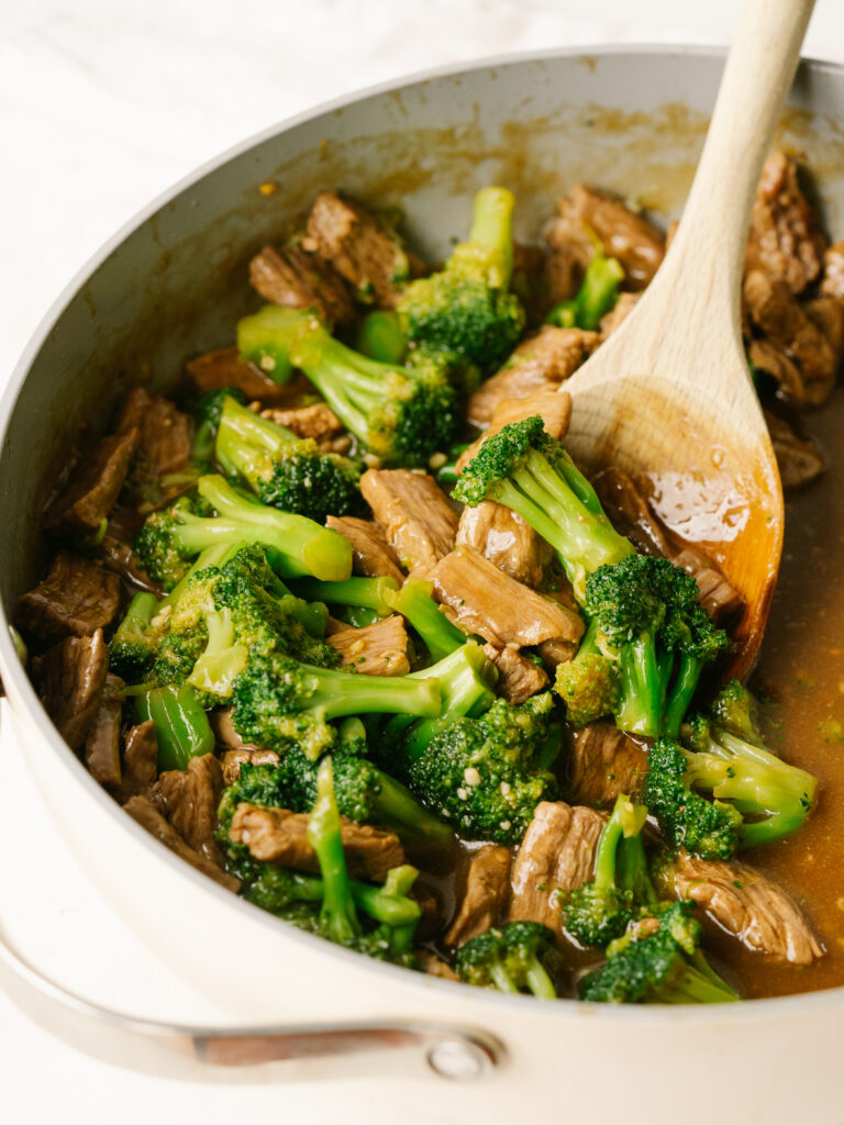 Three quarter view of easy beef and broccoli recipe in a pan with a wooden spoon