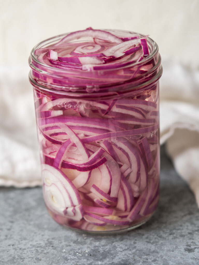 Thinly sliced red onions in a glass jar with pickling liquid poured on top