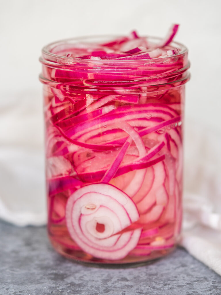 Side view of bright pink pickled red onions in a glass jar