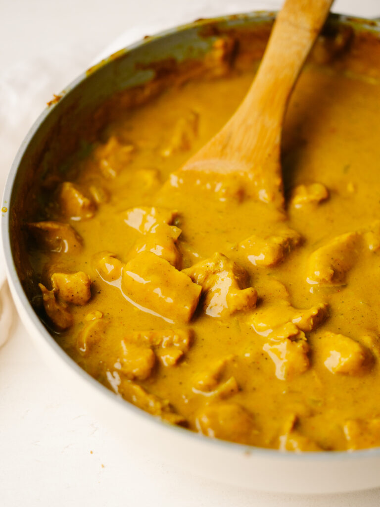 Three quarter view of pumpkin curry in a pan with a wooden spoon