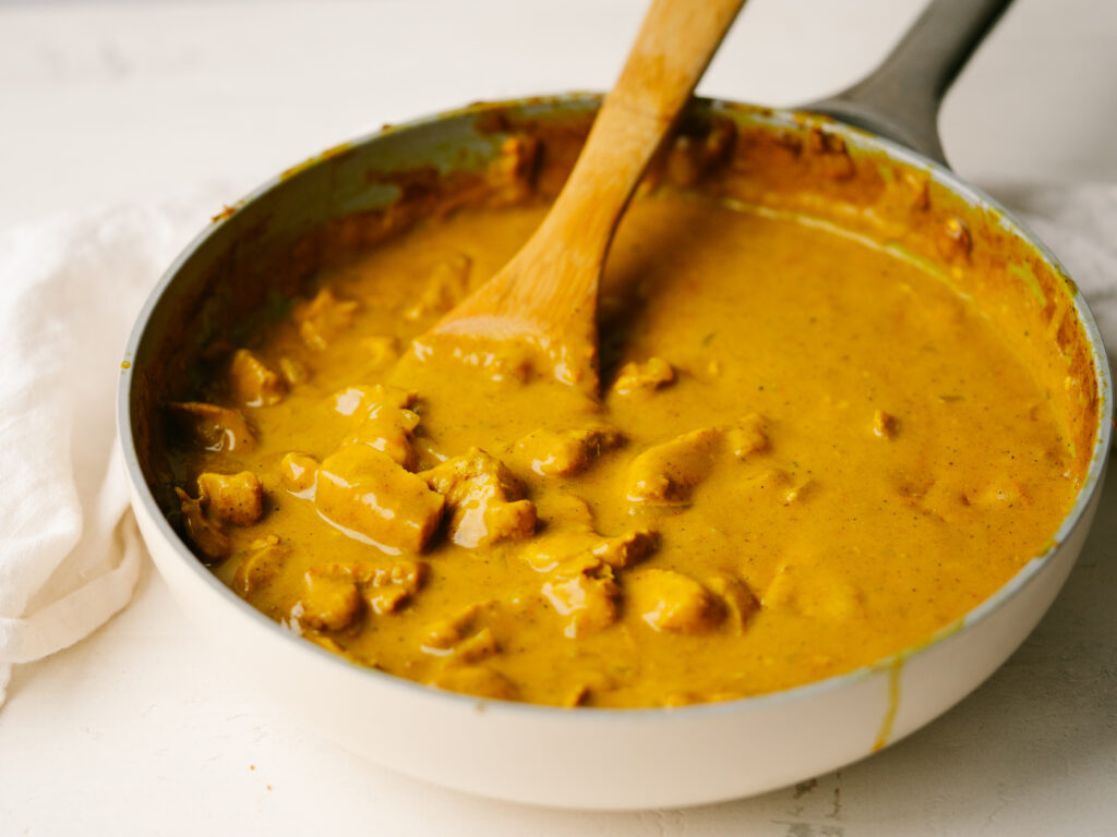 Three quarter view of pumpkin curry in a frying pan with a wooden spoon in it.