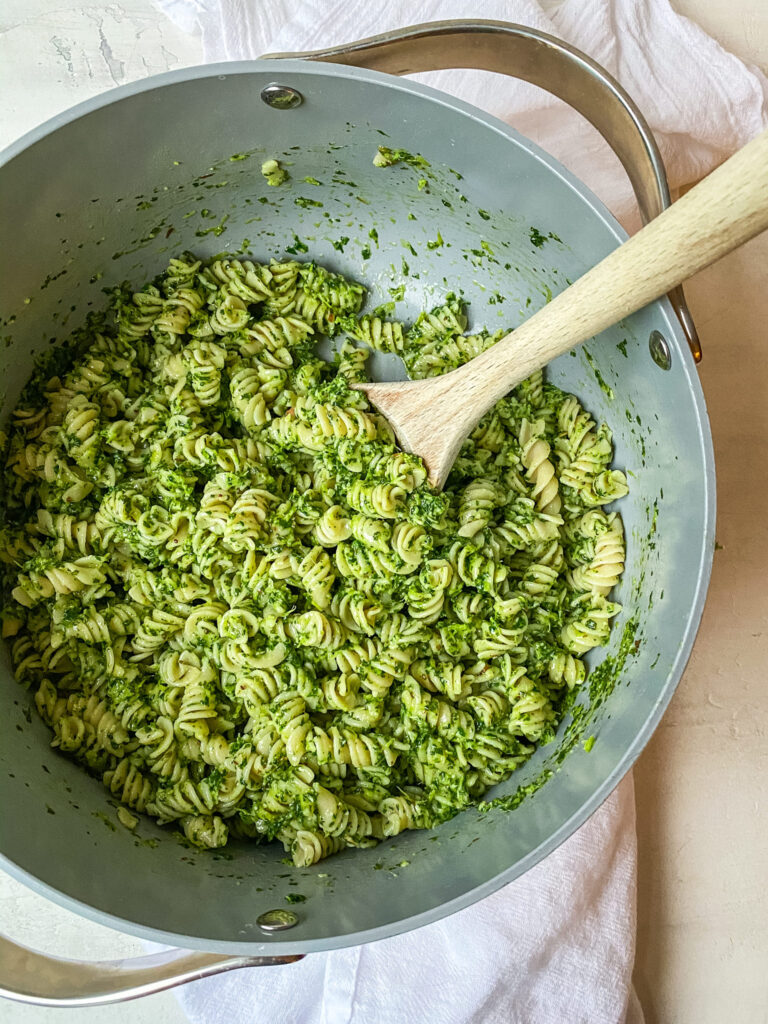 Above view of kale pesto pasta in a pot with a wooden spoon