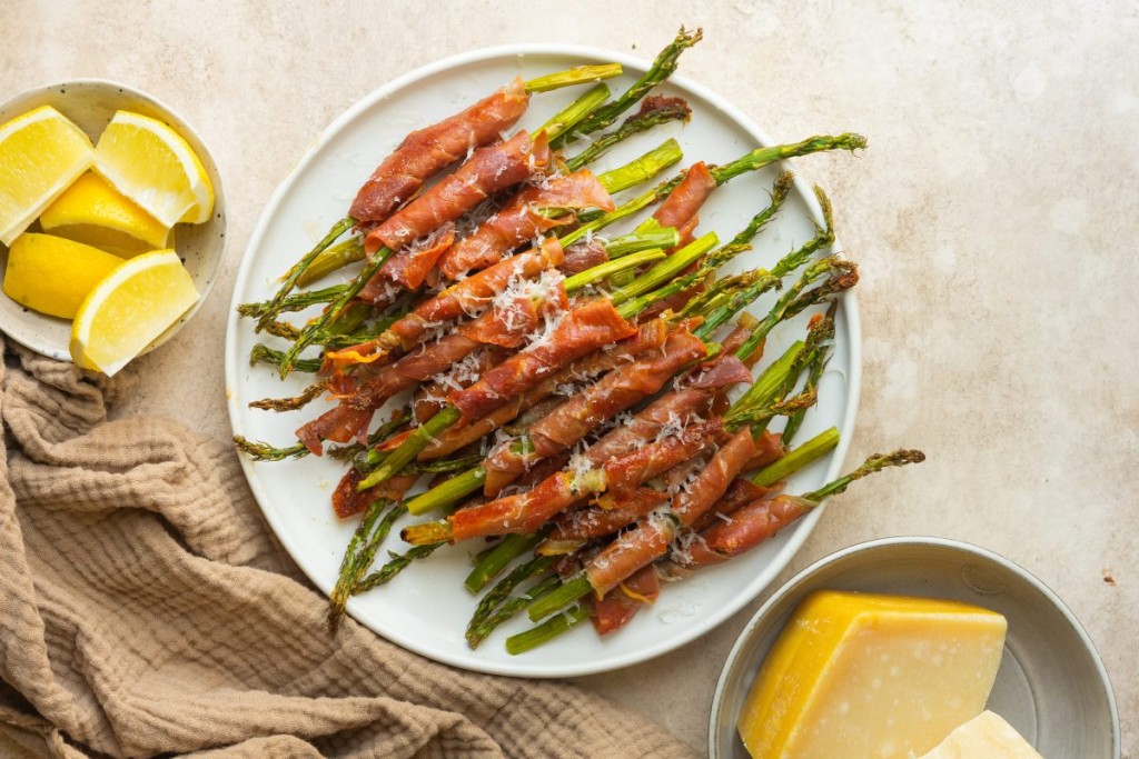 Above view of asparagus wrapped in prosciutto on a serve plate with parmesan cheese on top