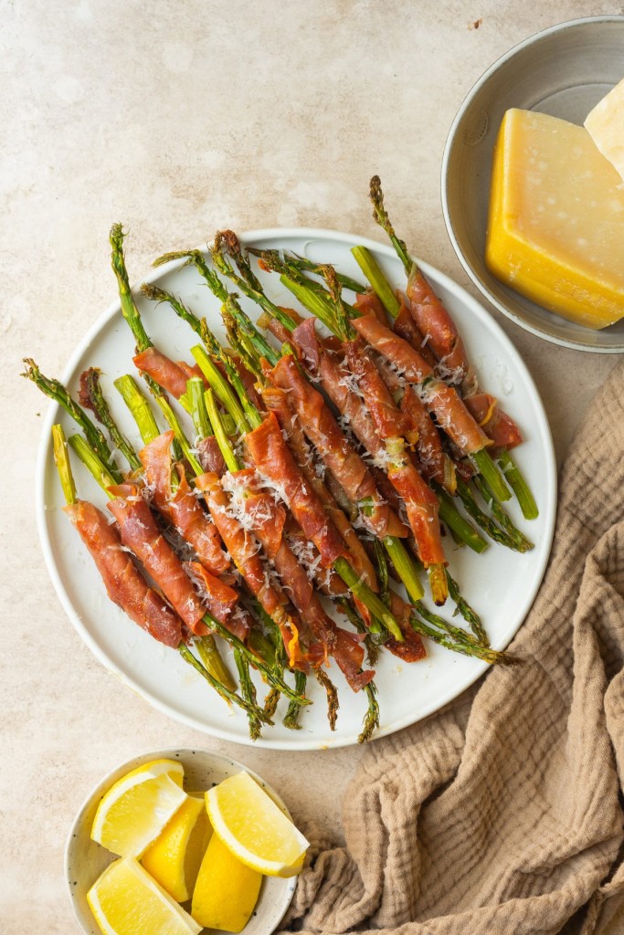 Above view of asparagus wrapped in prosciutto on a serve plate with parmesan cheese on top