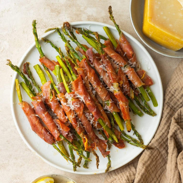Above view of asparagus wrapped in prosciutto on a serve plate with parmesan cheese on top