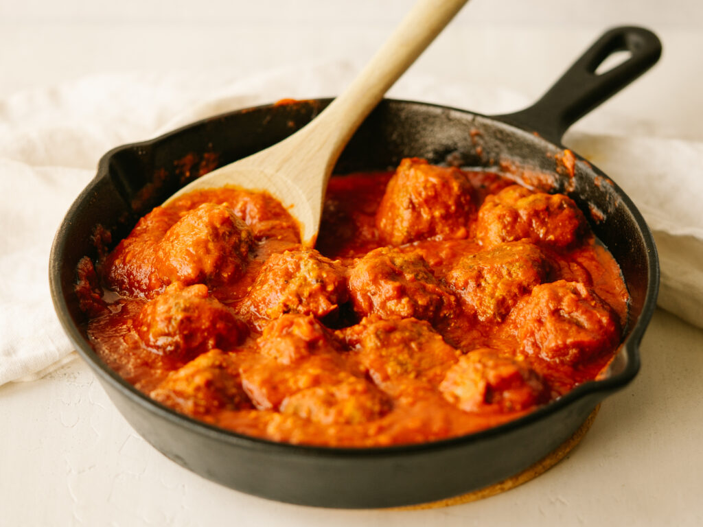 Three quarter view of meatballs in marinara sauce served in a cast iron skillet with a wooden spoon