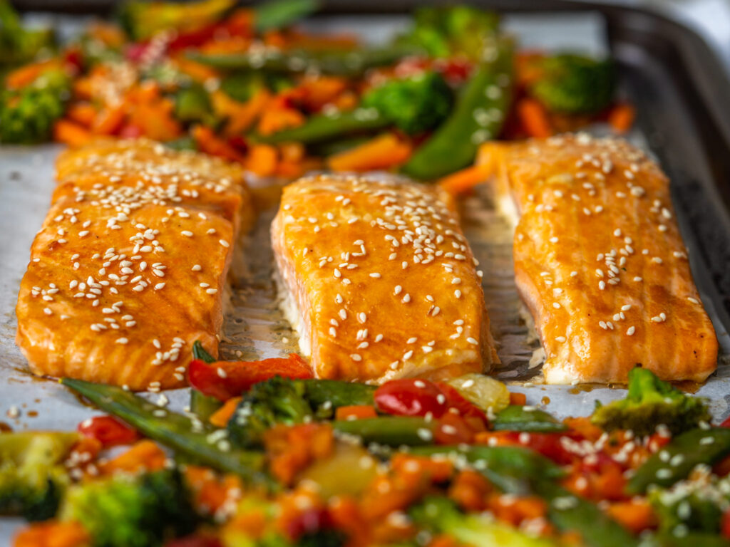 three quarter view of baked salmon filets on a sheet pan with veggies
