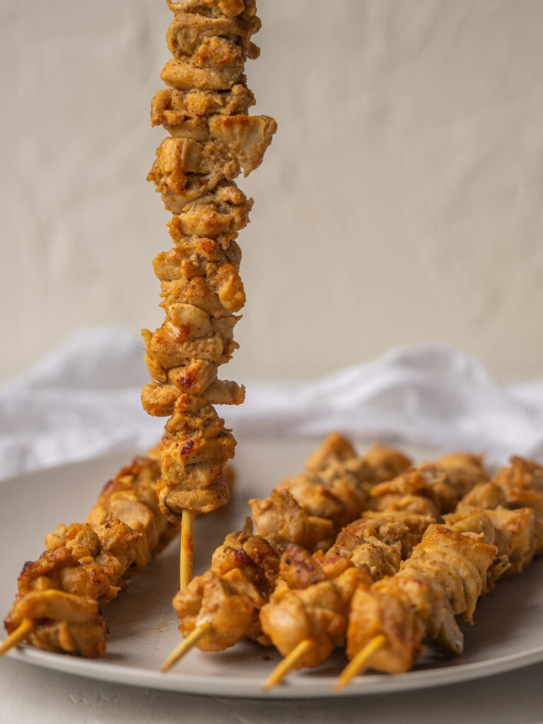 Side view of a  whole30 marinated chicken skewer standing up on a plate
