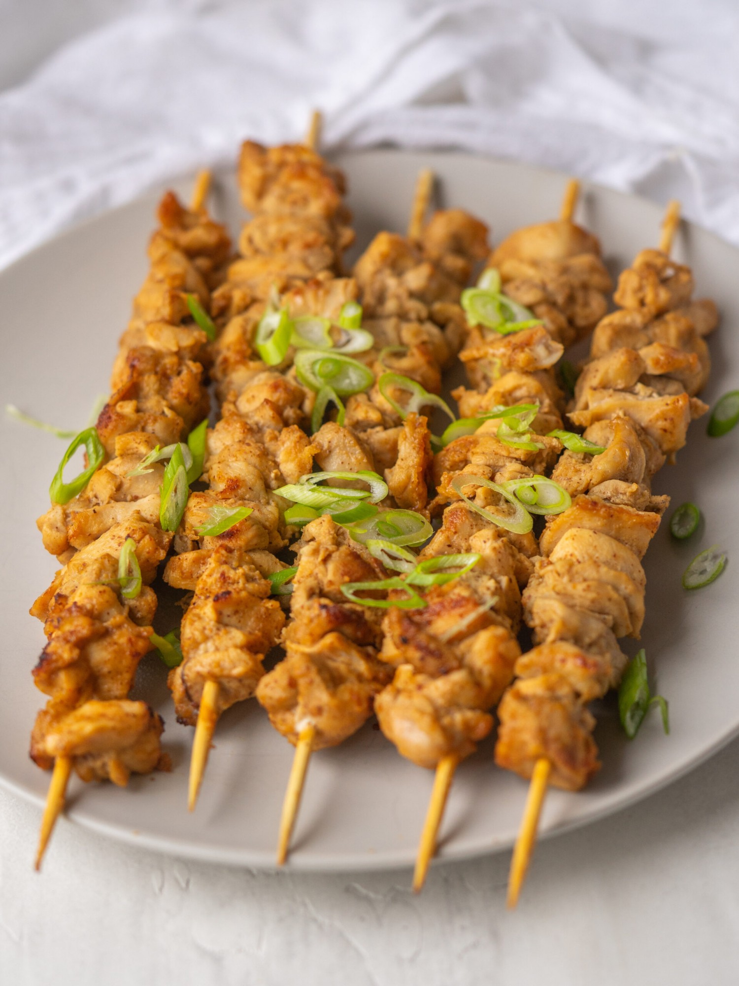 Three quarter view of almond butter chicken satay on a serving plate with green onion