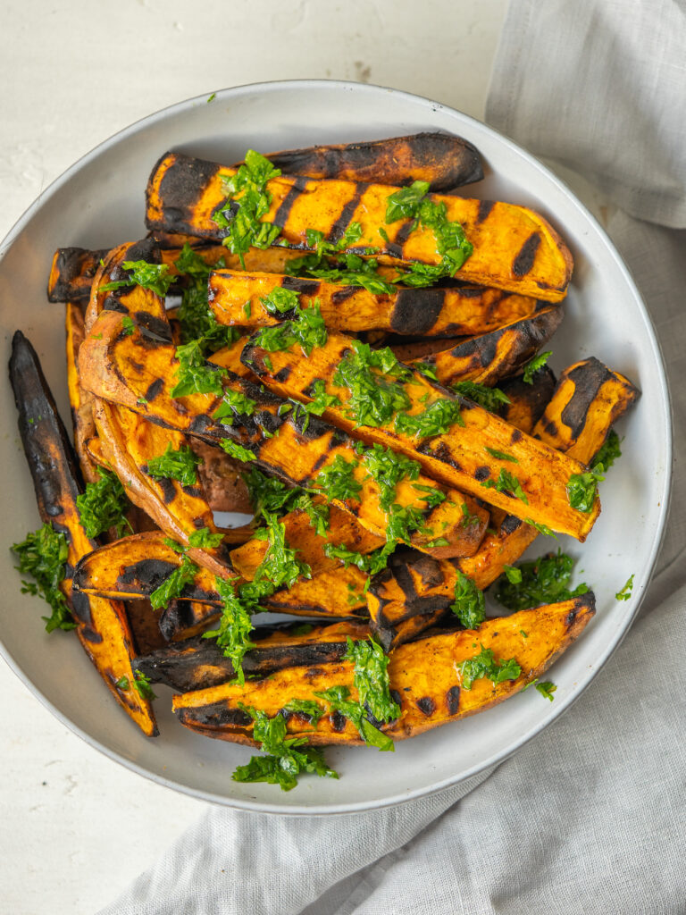 Above view of grilled sweet potatoes on a serving bowl with a mixed herb dressing