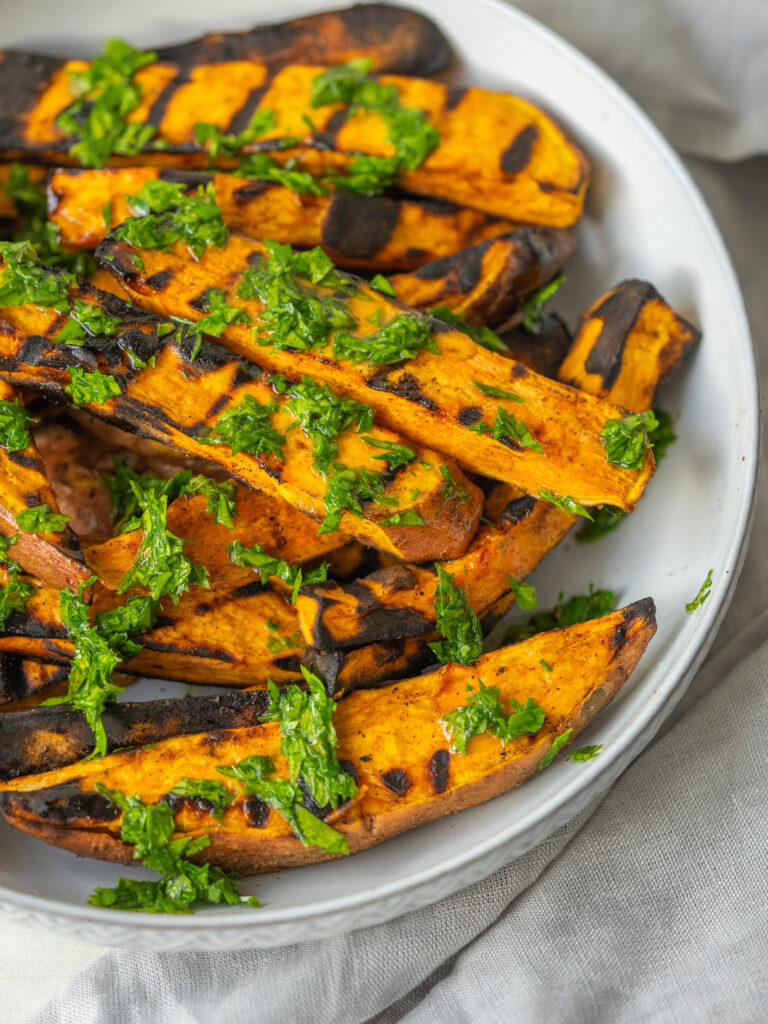 Close up three quarter view of grilled sweet potatoes with a mixed herb dressing