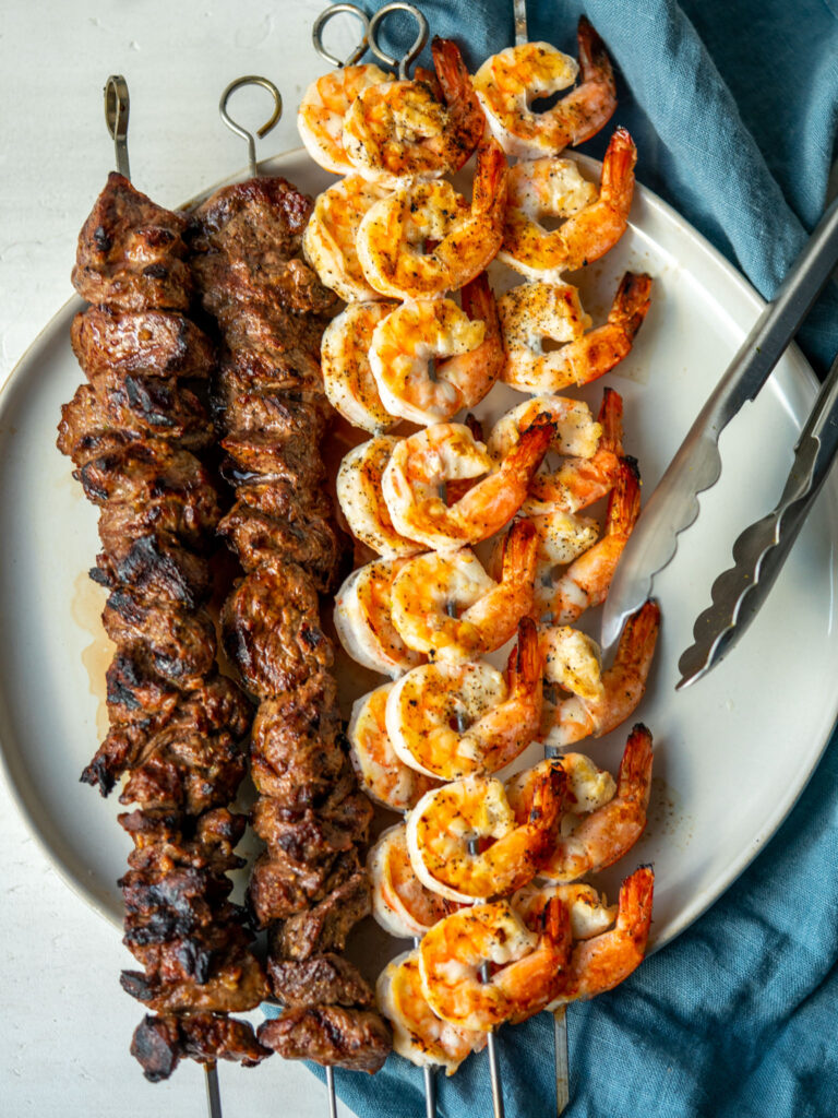 Above view of grilled surf and turf skewers on a plate with tongs