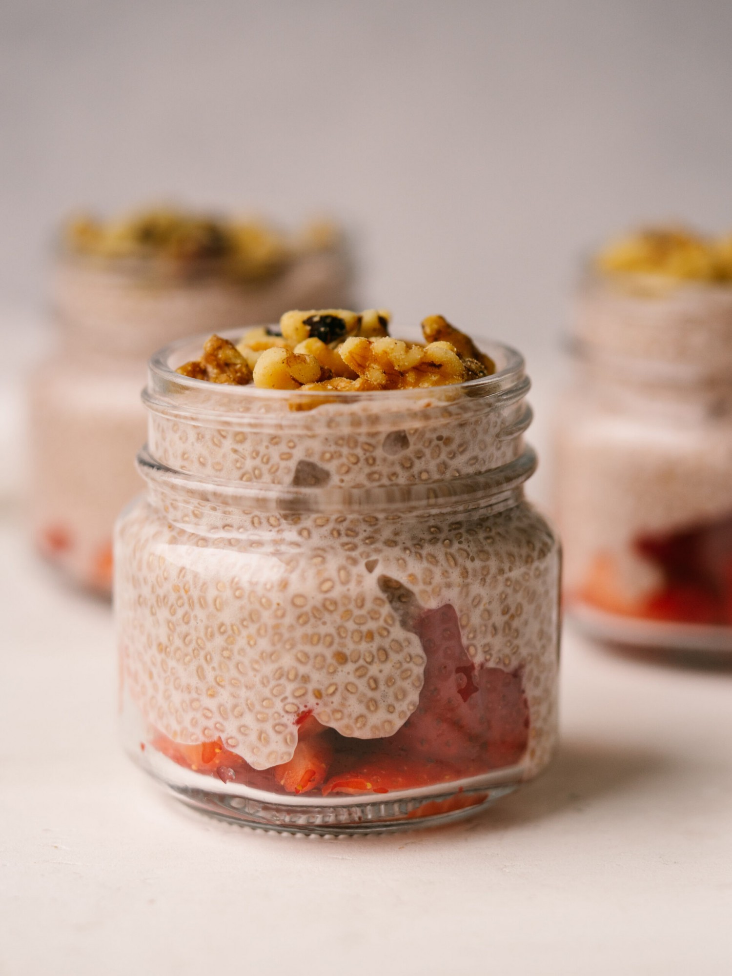 Side view of strawberry chia seed pudding in glass jars with fresh strawberries on the bottom of the jar and walnuts on top of the pudding