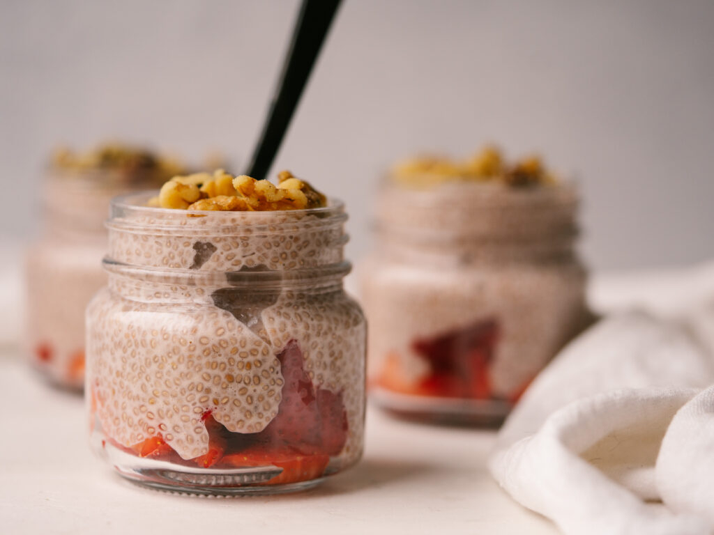 Side view of a jar of whole30 chia seed pudding with fresh strawberries and walnuts