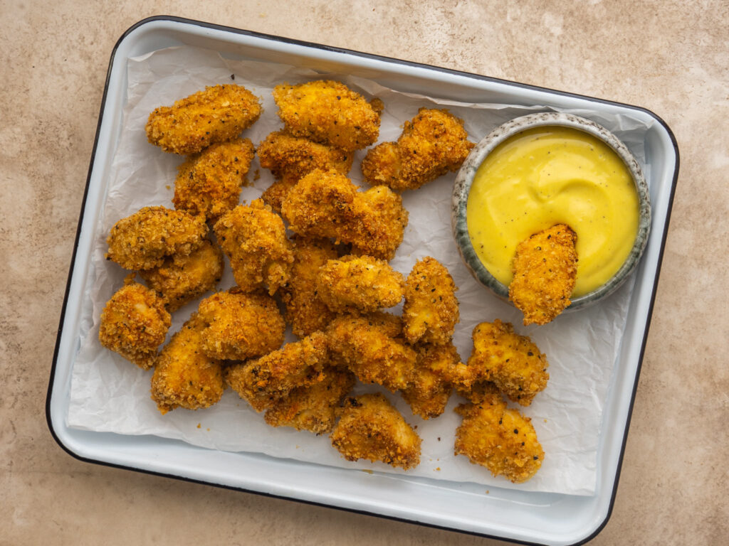 above view of chicken nuggets on a tray with one dipping into a sauce