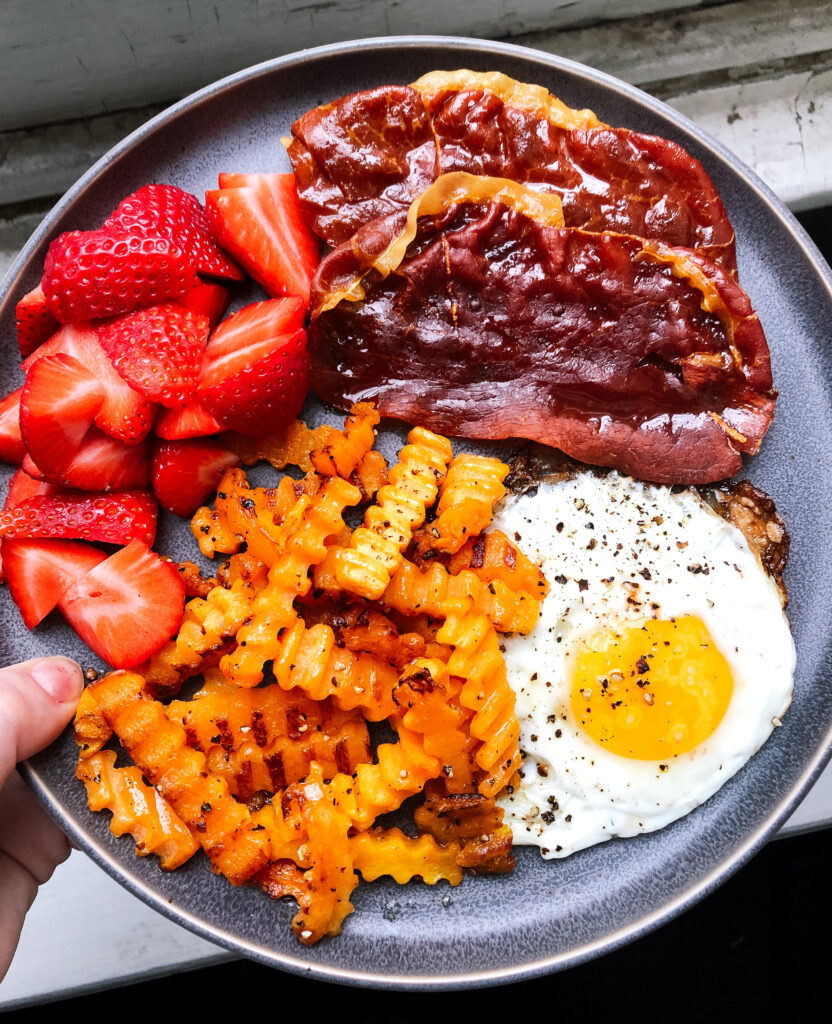 A breakfast plate with strawberries, crispy prosciutto, butternut squash and a fried egg