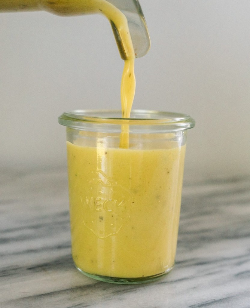 Side view of a white balsamic vinaigrette pouring from a blender into a small mason jar