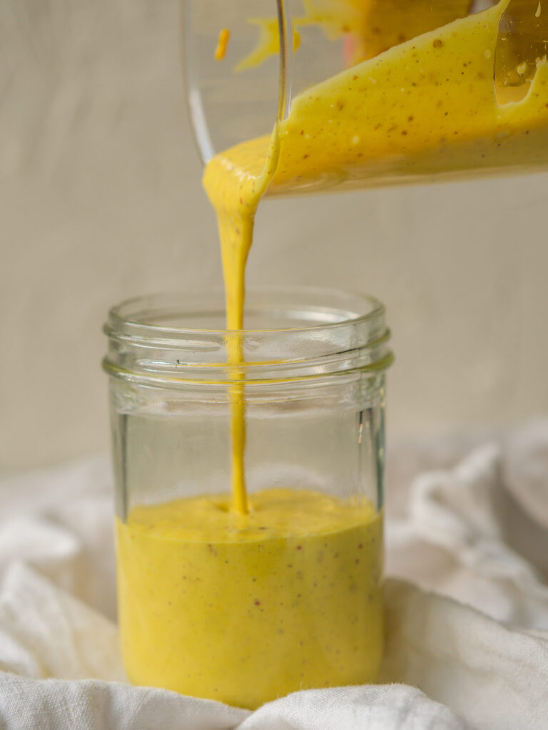 Side view of creamy honey mustard sauce pouring into a jar for storage