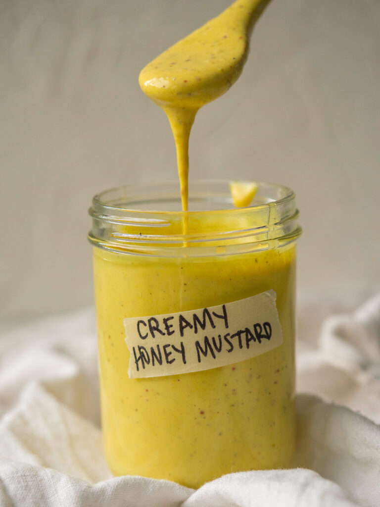 Side view of a spoon dipping into a jar labeled "creamy honey mustard"