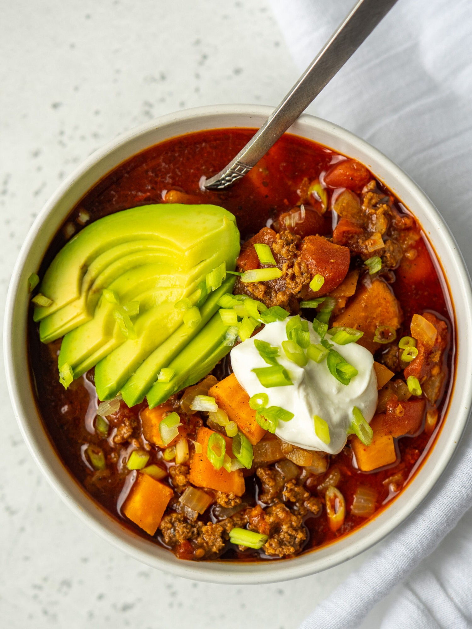Above view of sweet potato paleo chili in a bowl with avocado, sour cream and green onion