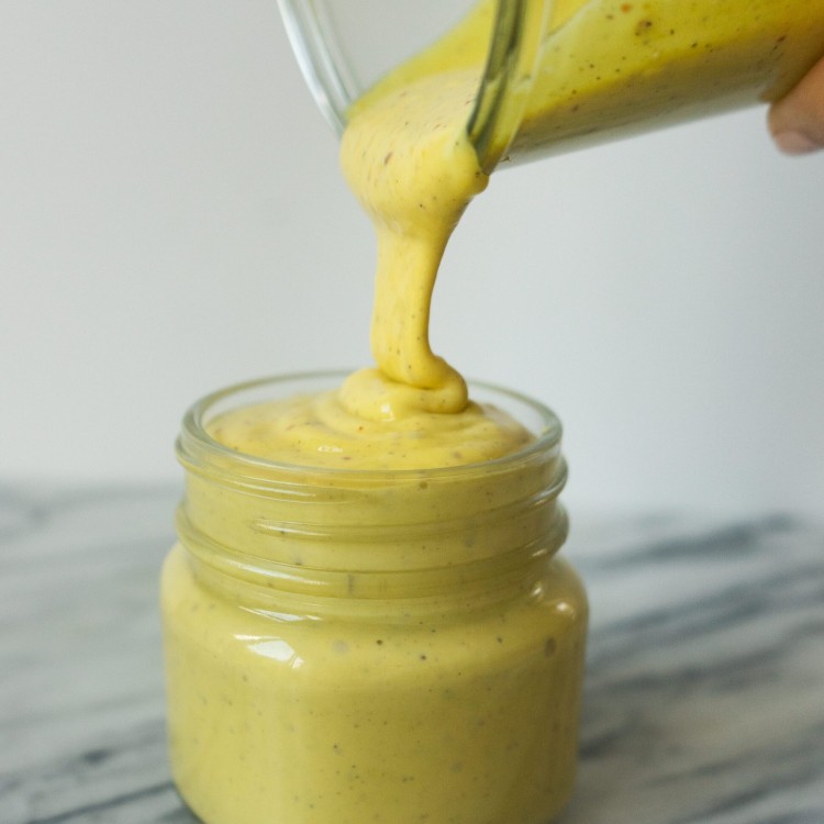 Side view of creamy honey mustard sauce pouring into a jar for storage