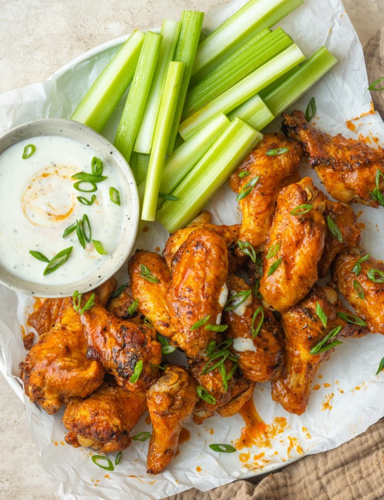 Air fryer buffalo wings garnished with green onion on a plate with celery and ranch dressing