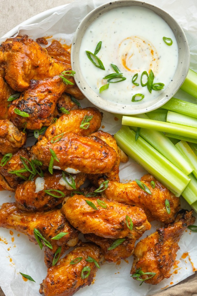 close up view of air fryer buffalo wings garnished with green onion on a plate with celery and ranch dressing