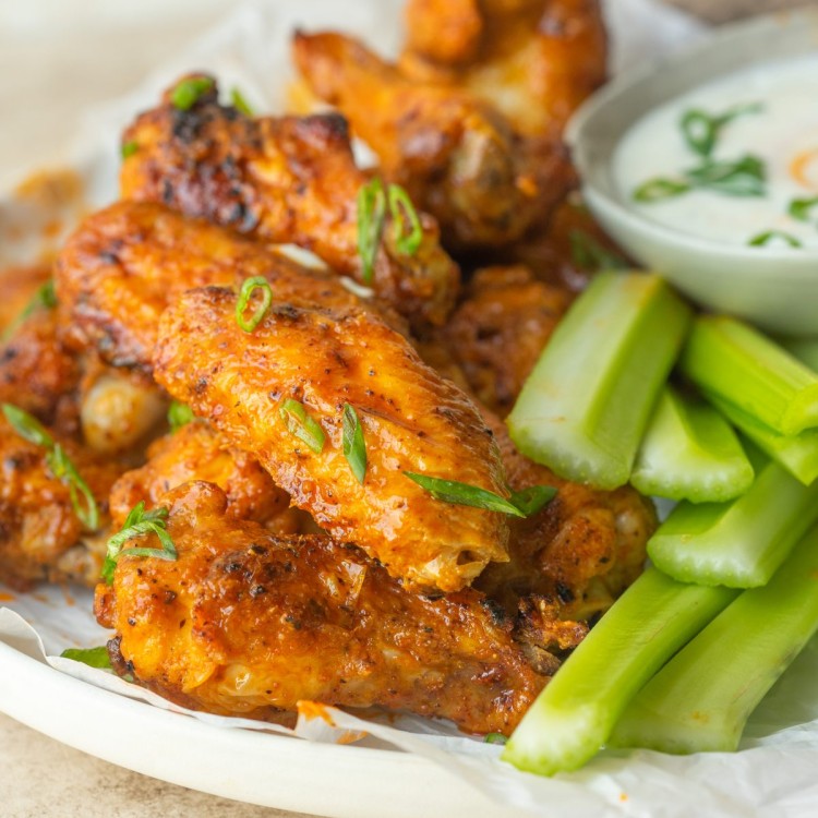 Three quarter view of buffalo wings stacked on a serving plate next to celery and ranch for dipping