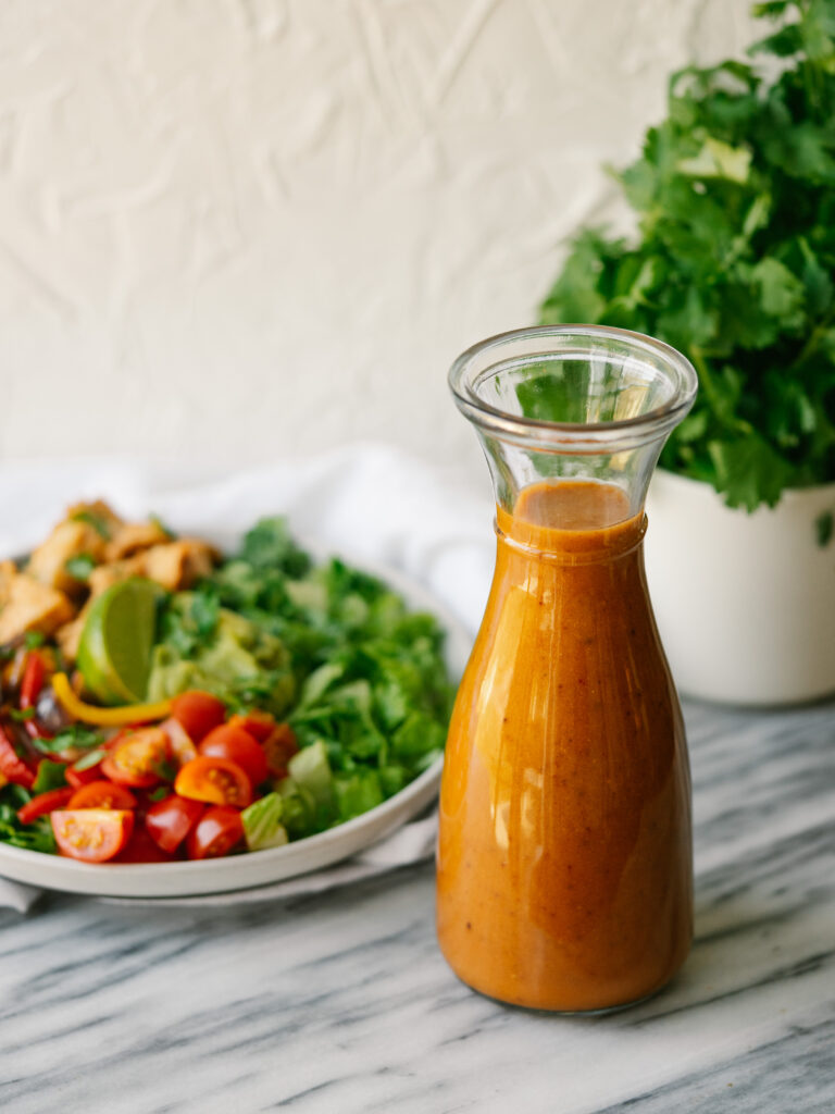 chipotle vinaigrette in a glass bottle in front of a salad and herbs