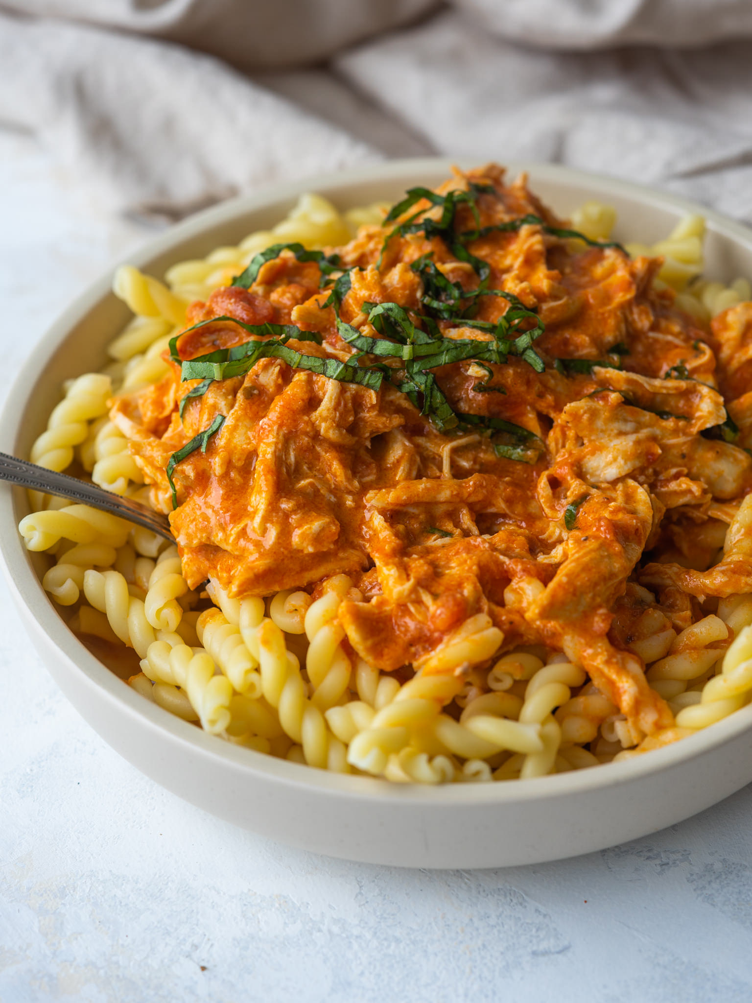 a three quarter view photo of creamy shredded chicken pasta sauce on pasta in a white bowl