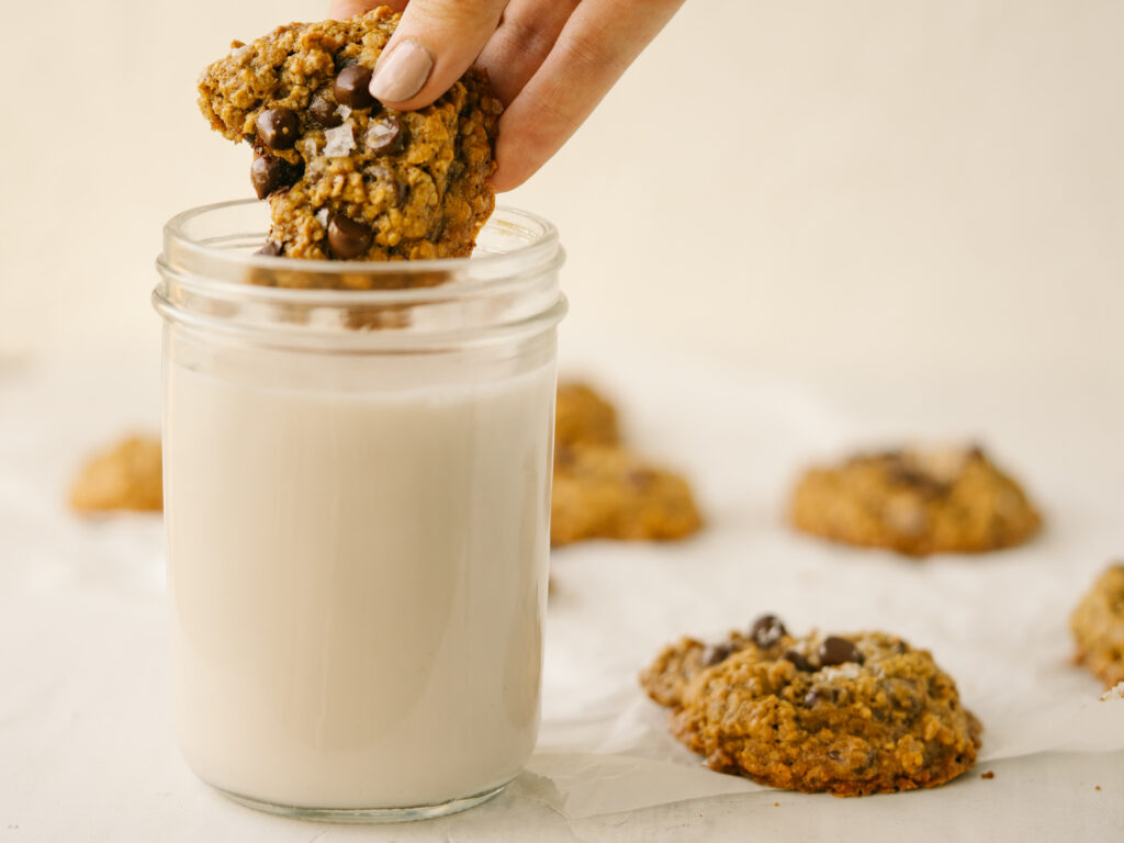 Side view of a healthy peanut butter oatmeal cookie dipping into a glass of milk