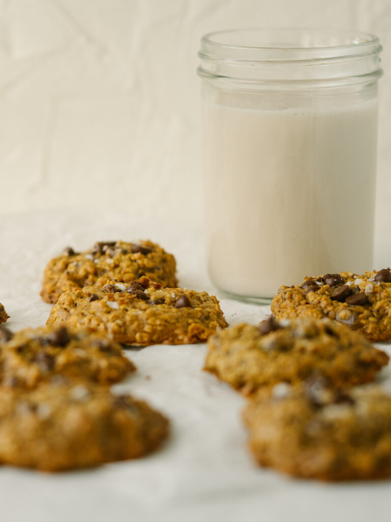 Side view of healthy peanut butter oatmeal cookies on a piece of parchment paper next to a glass of milk