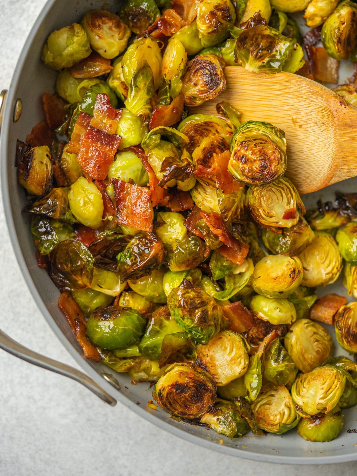 Above view of maple bacon brussels sprouts in a frying pan with a wooden spoon