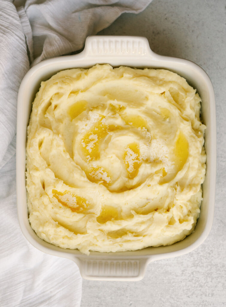 Above view of creamy mashed potatoes in a serving dish with melted butter on top