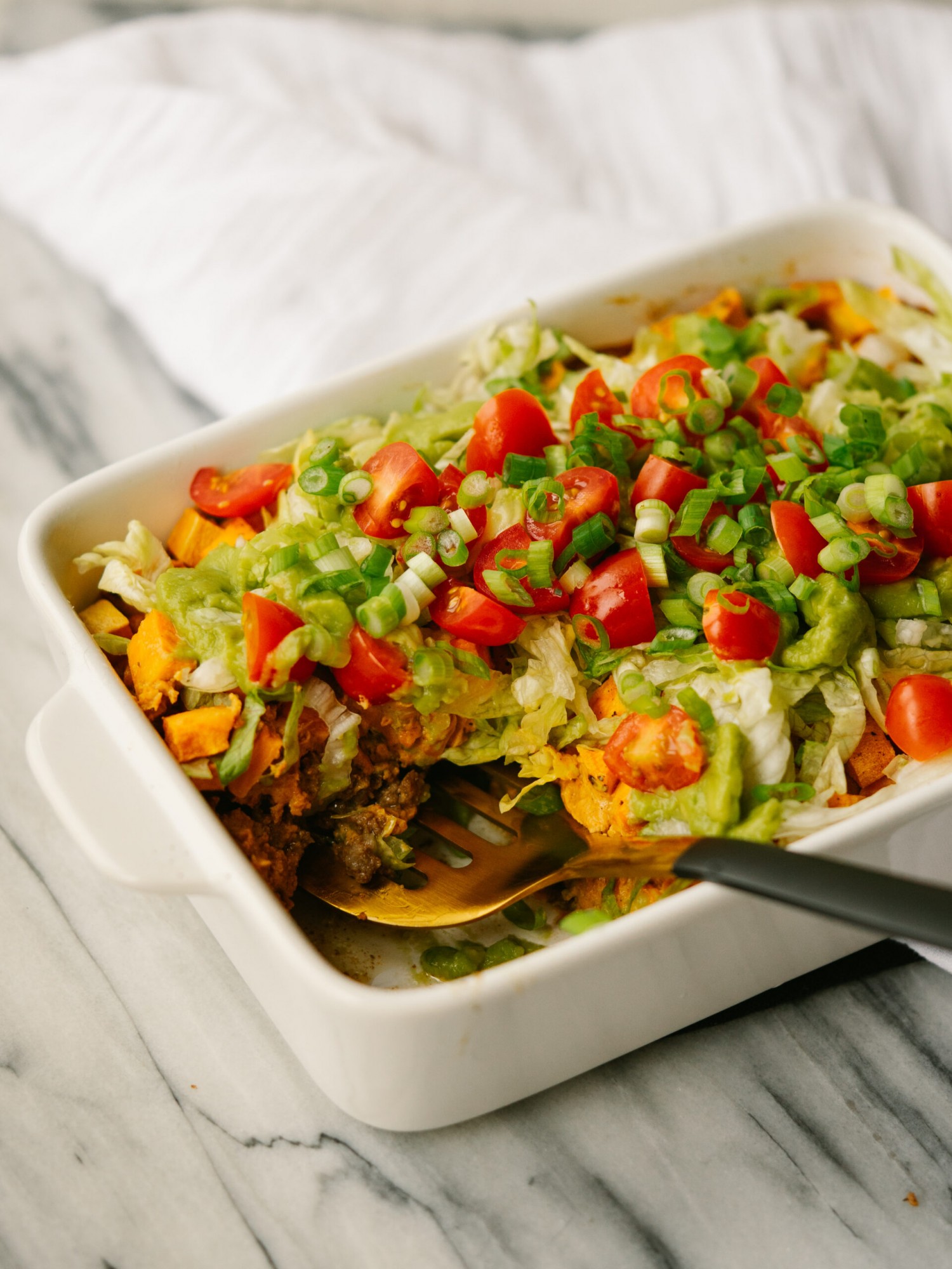 Three quarter view of a casserole with a taco base topped with sweet potatoes, lettuce and tomatoes