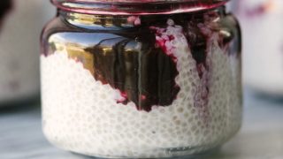 Side view of coconut chia seed pudding in a glass jar with blueberry compote on top