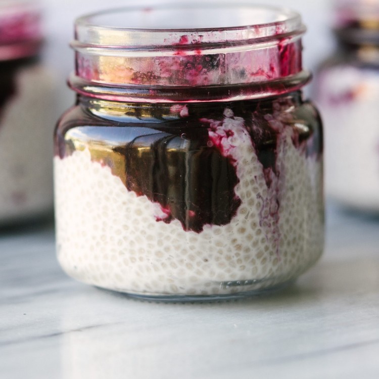 Side view of coconut chia seed pudding in a glass jar with blueberry compote on top