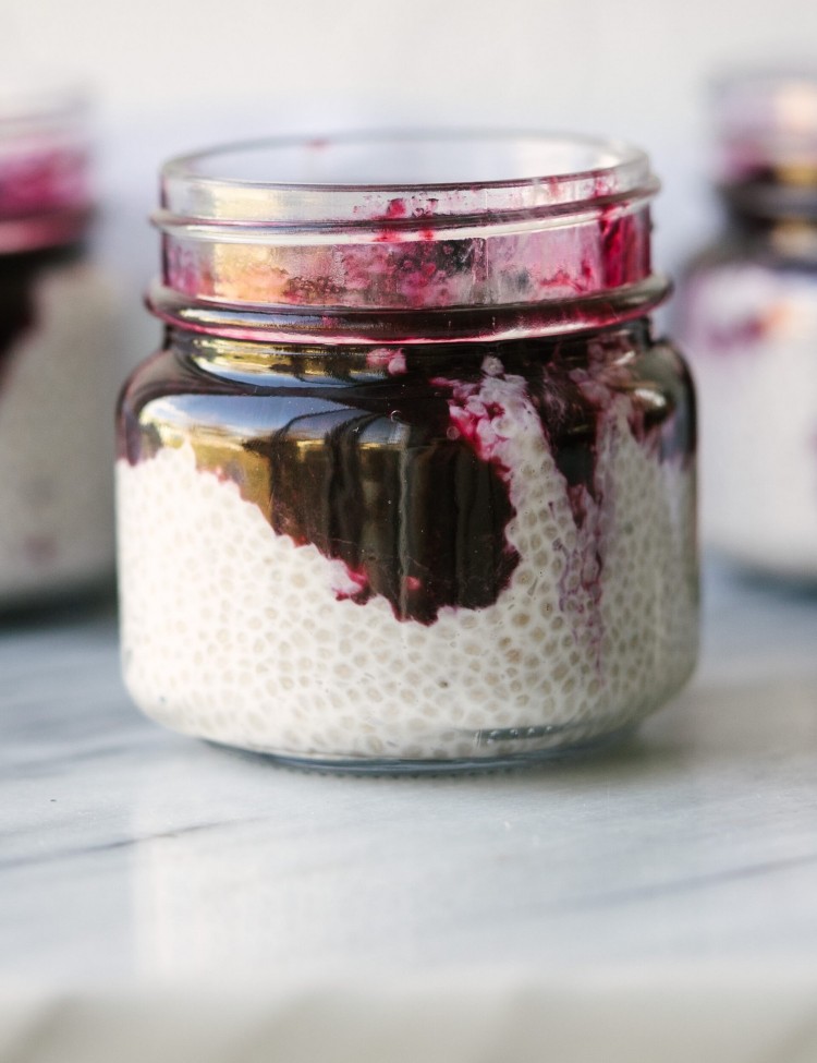 Side view of coconut chia seed pudding in a glass jar with blueberry compote on top