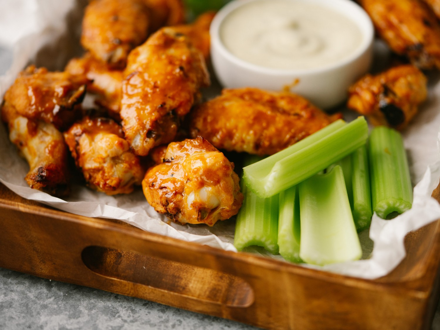 a side view photo of orange chicken wings with celery and ranch on a platter
