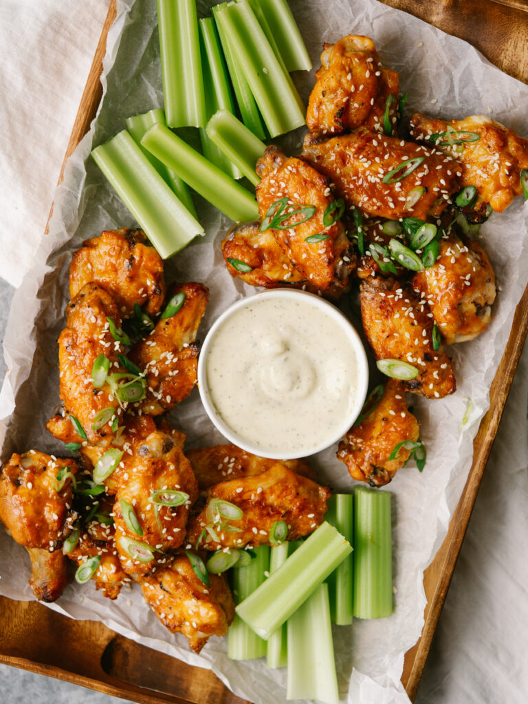 an above view photo of orange chicken wings on a platter with celery and ranch