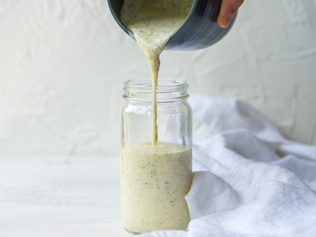 Side view of dairy free ranch dressing pouring into a glass storage jar