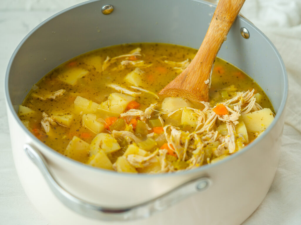 Three quarter view of Greek lemon soup in a stock pot with a wooden mixing spoon in it 
