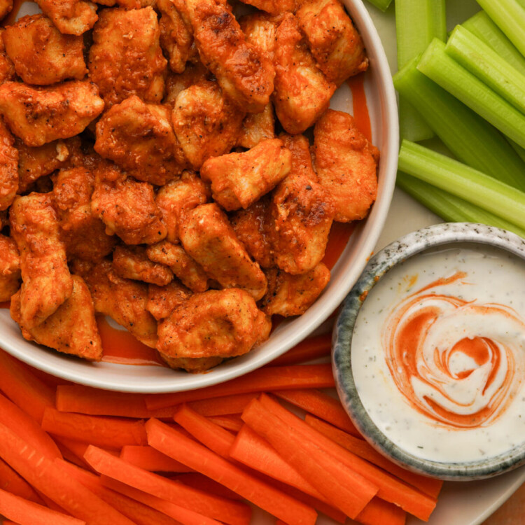 an above view photo of buffalo chicken bites in a bowl surrounded by celery and carrots and a small bowl of ranch dressing