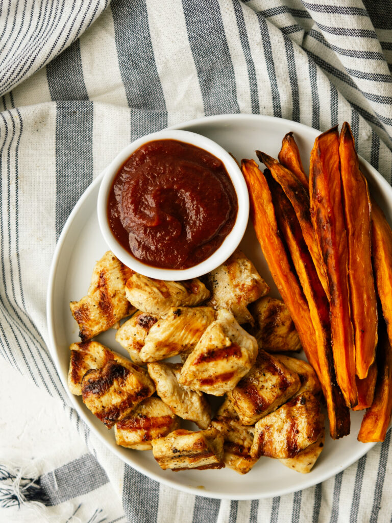 an above view image of grilled nuggets with sweet potato fries with a small bowl of ketchup