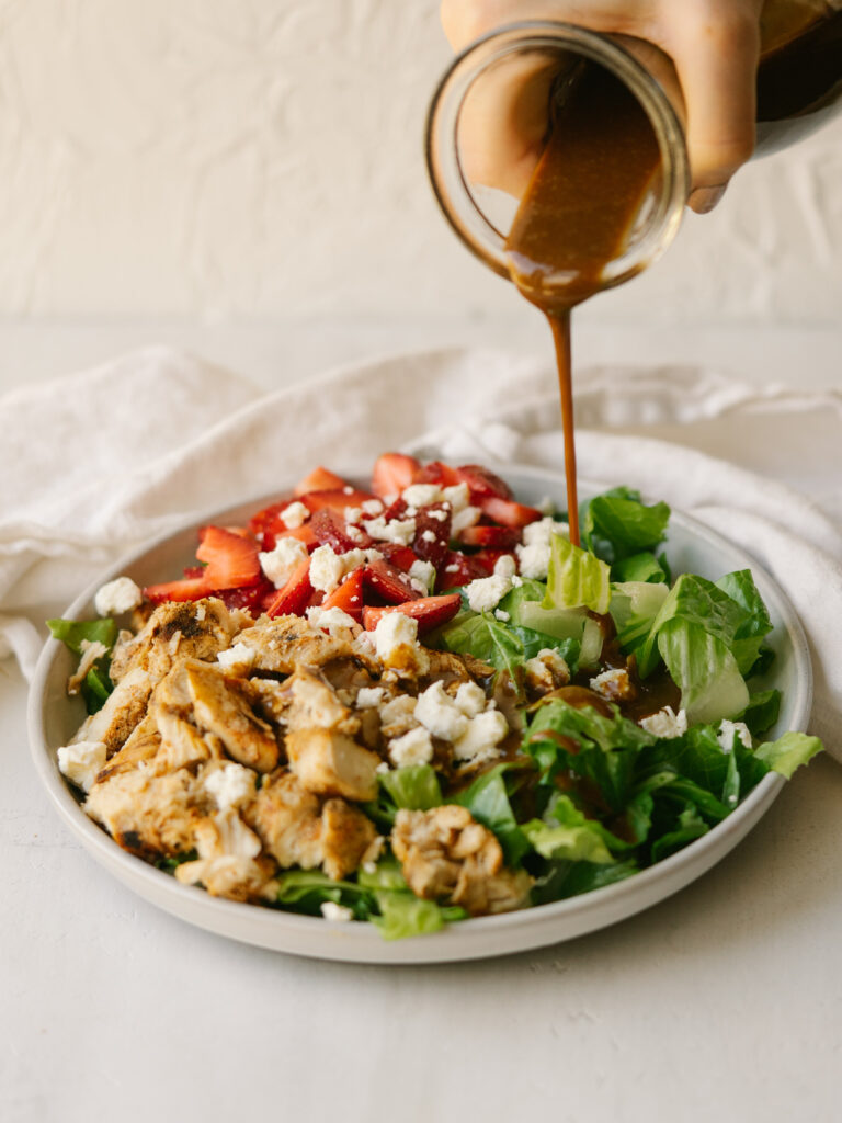 three quarter view of balsamic dressing pouring onto  a salad with chicken and strawberries