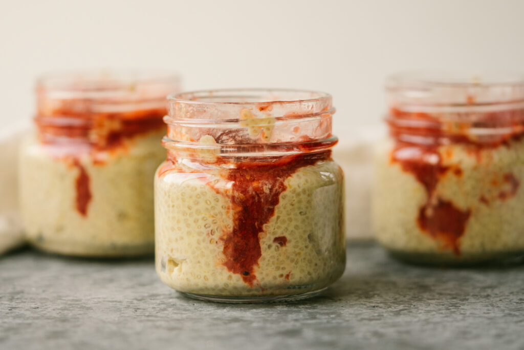Side view of strawberry mango chia seed pudding in small glass jars on a grey counter