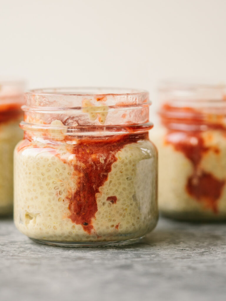 Side view of mango chia pudding in a glass jar with strawberry compote swirled into the pudding