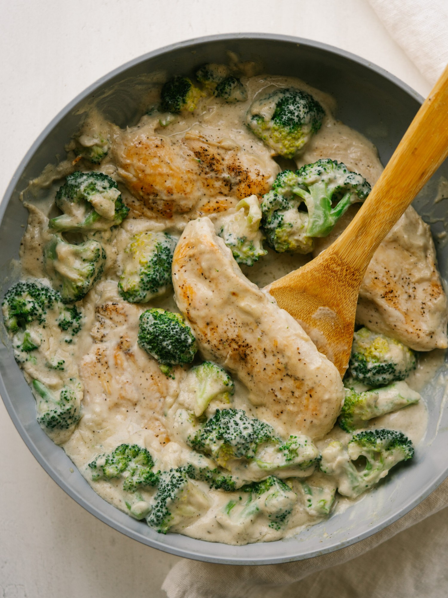 an above view photo of chicken and broccoli in cashew sauce in a pan with a wooden spoon in it