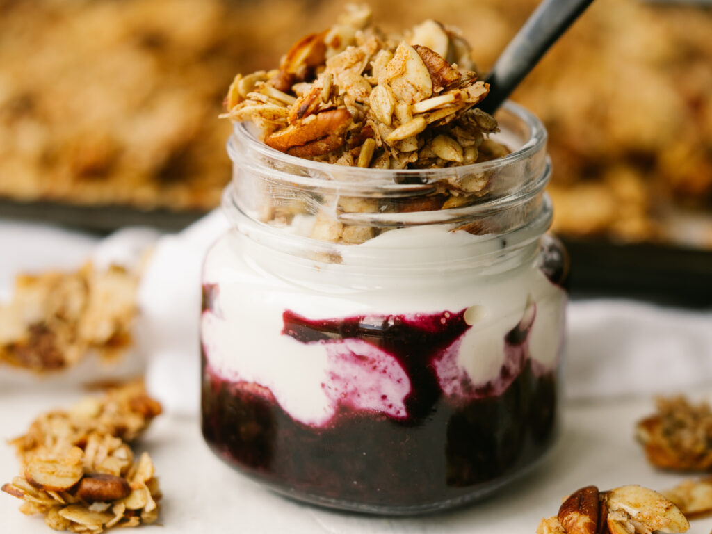 Side view of maple cinnamon grain free granola on yogurt and berries in a glass jar